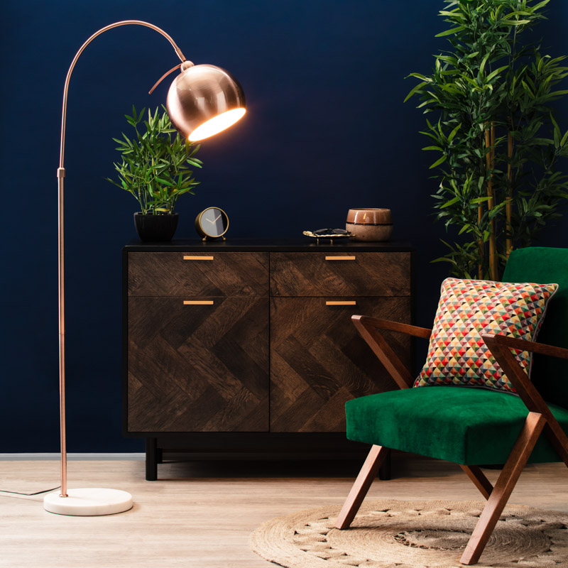 copper, curved floor lamp styled by a chair.